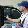 Worker washing tinted car window in workshop